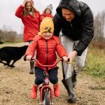 A joyful scene of a father helping his child ride a bike outdoors.